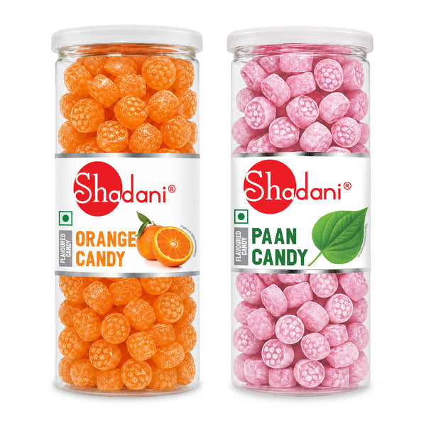 Two clear plastic jars of Shadani flavored candy on a white background. The left jar contains orange grape-shaped candy labeled 'Orange Candy', and the right jar contains pink cube-shaped candy labeled 'Paan Candy'.