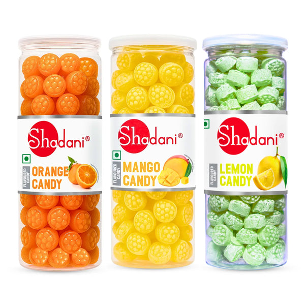 Three clear plastic jars of Shadani candies on a white background: orange round candies labeled Orange Candy, yellow round candies labeled Mango Candy, and light green cube-shaped candies labeled Lemon Candy.