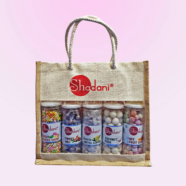 A burlap tote bag with the Shadani brand logo, containing various packaged sweets and snacks.