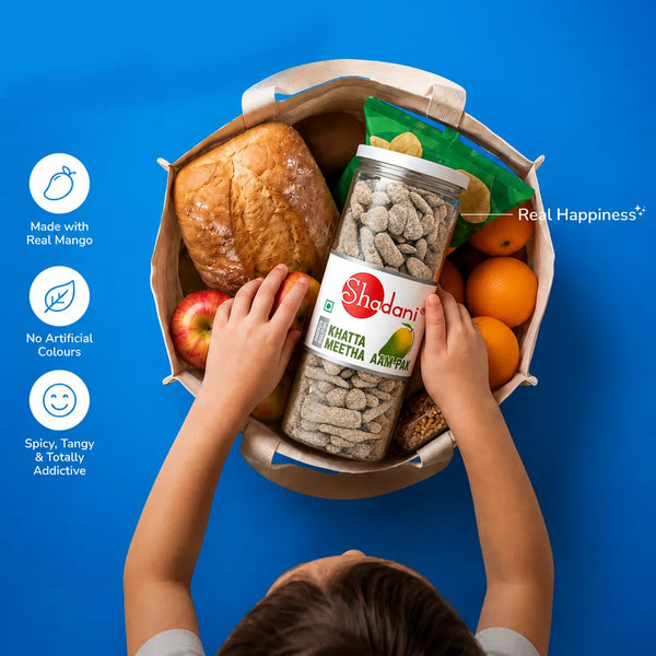Child's hands holding a jar of Shadani snacks above a basket with bread, apples, and oranges on a blue background.