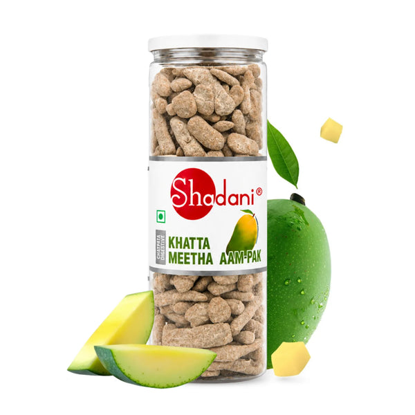 A clear plastic jar of Shadani Khatta Meetha Aam-Pak with a white label, shown on a white background with sliced green mangoes and small yellow fruit pieces around it.