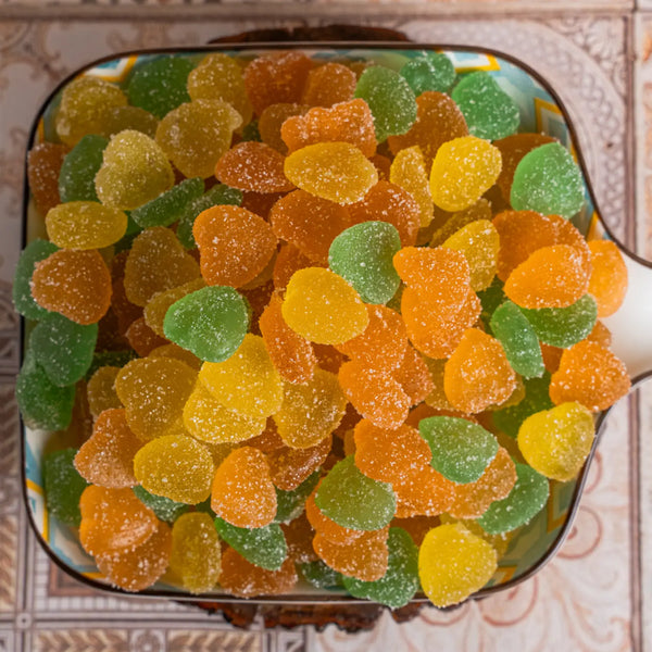 Assorted colored shadani jelly gummy bears in a container on a patterned surface