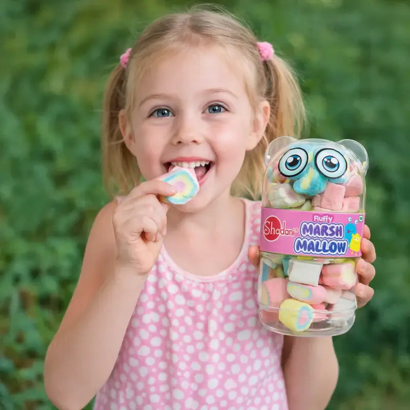 Young girl holding a container of colorful shadani marshmallows with a green leafy background