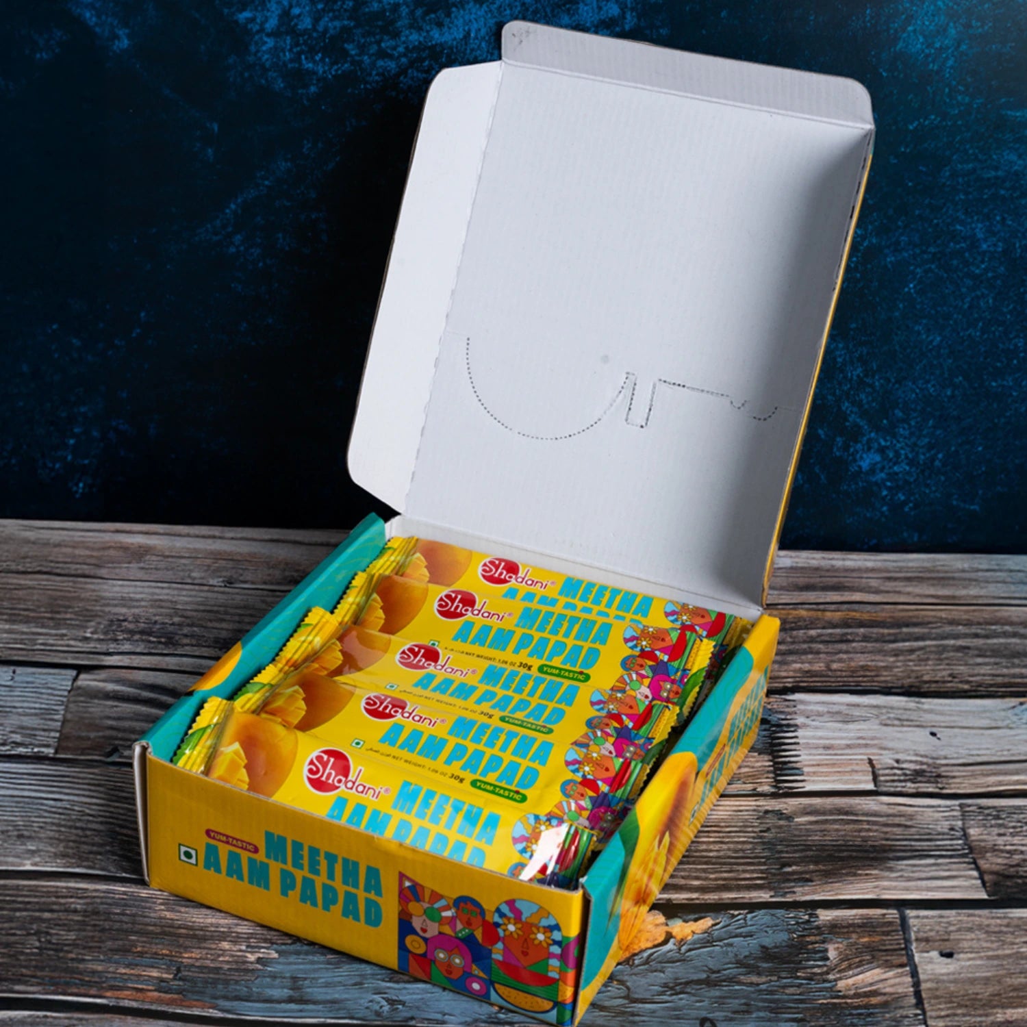 Open a box of shadani meetha aampapad with colorful packaging on a wooden surface.