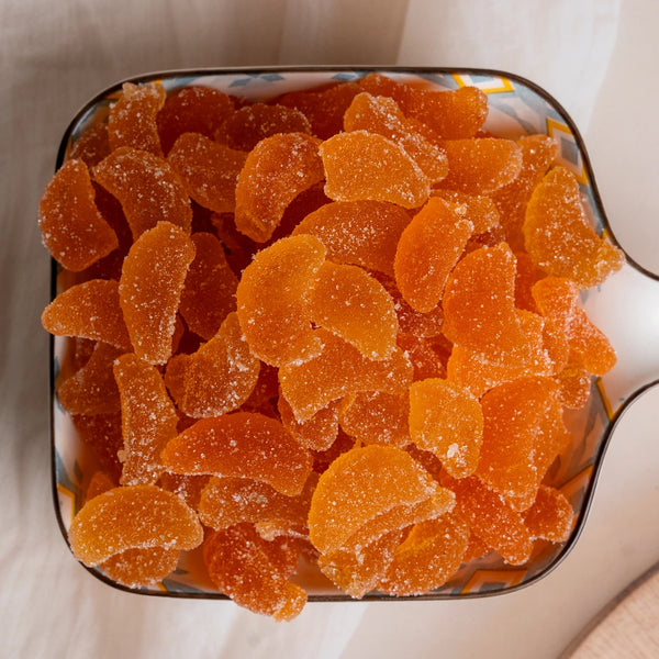Metallic container filled with orange gummy bears on a white surface