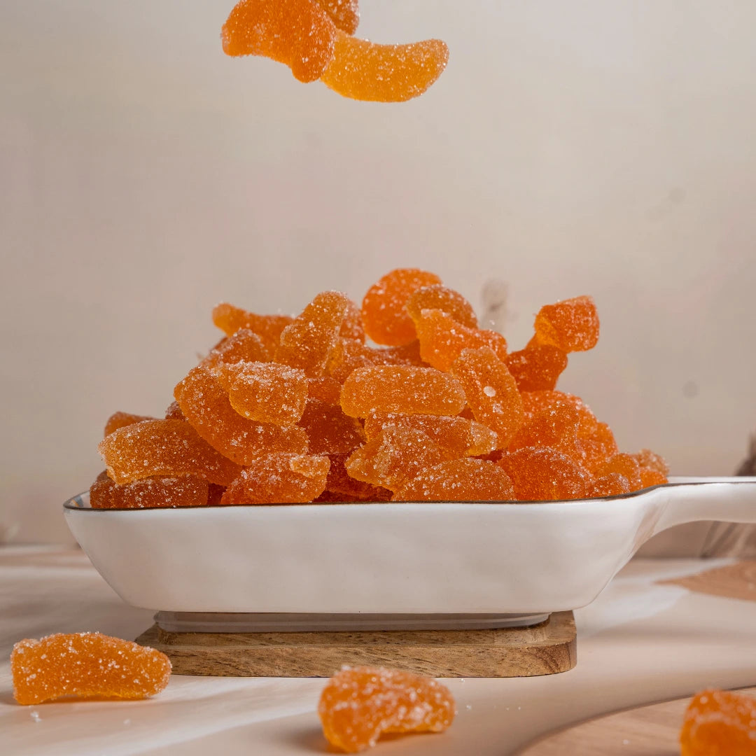 Orange gummy bears in a white bowl on a wooden surface with a neutral background