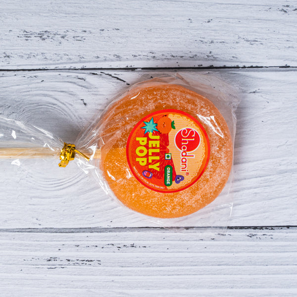 Orange jelly lollipop with a Shadan! label on a white wooden surface