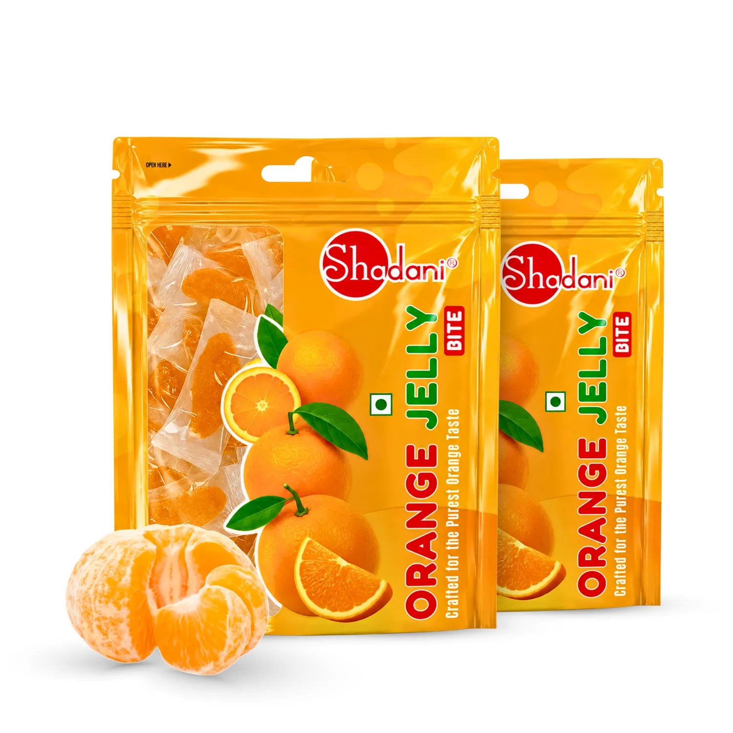 Two bags of Shadani Orange Jelly Bite candies with fresh orange slices and peeled mandarin segments in front, on a clean white background.