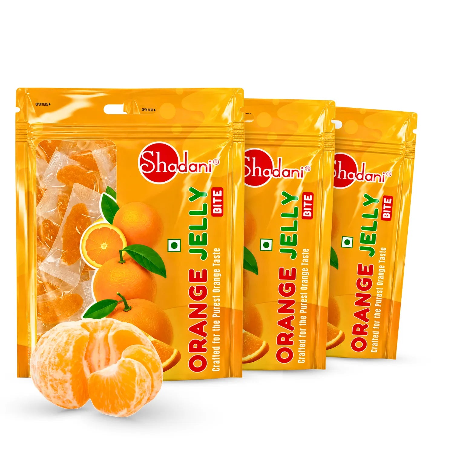 Three bags of Shadani Orange Jelly Bite candies arranged in a fan shape on a white background, with a whole mandarin and sliced mandarin pieces placed in front of the bags.