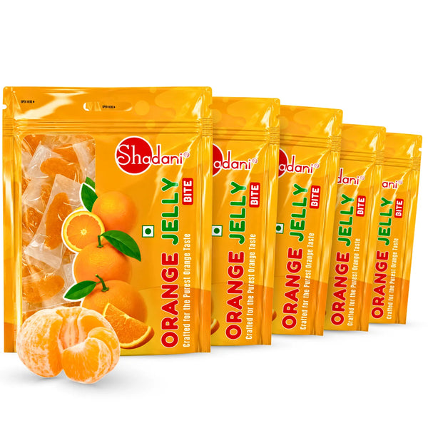 Five packages of Shadani Orange Jelly Bite candies arranged in a row on a white background, with a loose orange jelly candy piece in the foreground.