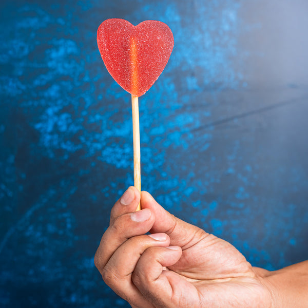 Hand holding a red heart-shaped lollipop against a blue textured background